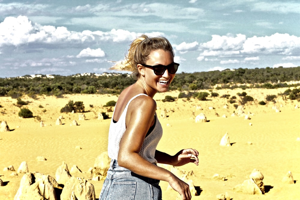 women's in white tank top walking on brown sand during day time