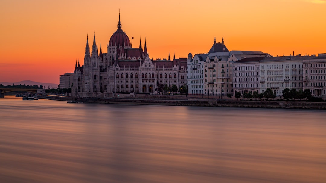 white and red concrete building near body of water, This image features the parliament building in Budapest, Hungary. In the early summer months the ambient light from the sunrise begins around 4am offering a soft glow of light for an extended period of time. The orange sky and soft color of the water give me a sense of calmness and tranquility.<p></figure>Enjoy:)