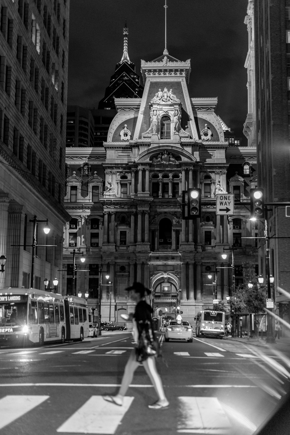 Fotografía en escala de grises de un hombre caminando por el carril peatonal cerca de un edificio de gran altura