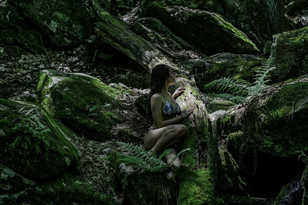 A woman in a bikini among mossy logs and rocks in a forest in Wilton