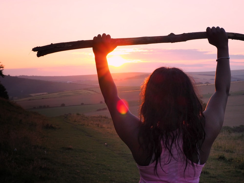 femme portant un débardeur rose tenant un bâton de bois au lever du soleil