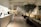 A modern, elegant hotel lobby with a minimalist design features a long reception counter on the left. Several people are working behind the counter. There are large potted plants, contemporary art sculptures, and soft lighting from stylish lamps scattered throughout the space. Comfortable seating areas with beige cushions are arranged on the right side.
