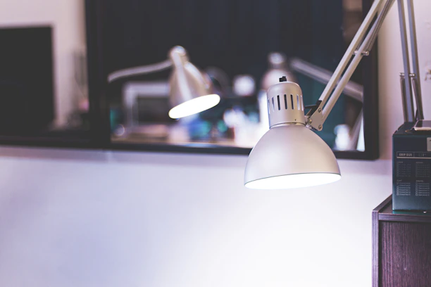 Close-up of a modern İşıkça table lamp glowing warmly on a wooden desk.