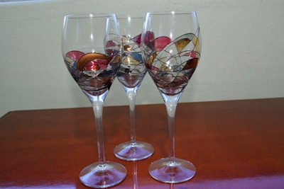A set of wine glasses decorated with vibrant resin designs sitting on a wooden table.