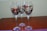 Three wine glasses with decorative colored patterns are placed on a wooden surface. The design features abstract shapes in shades of red, gold, and black.