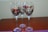 Three wine glasses with decorative colored patterns are placed on a wooden surface. The design features abstract shapes in shades of red, gold, and black.