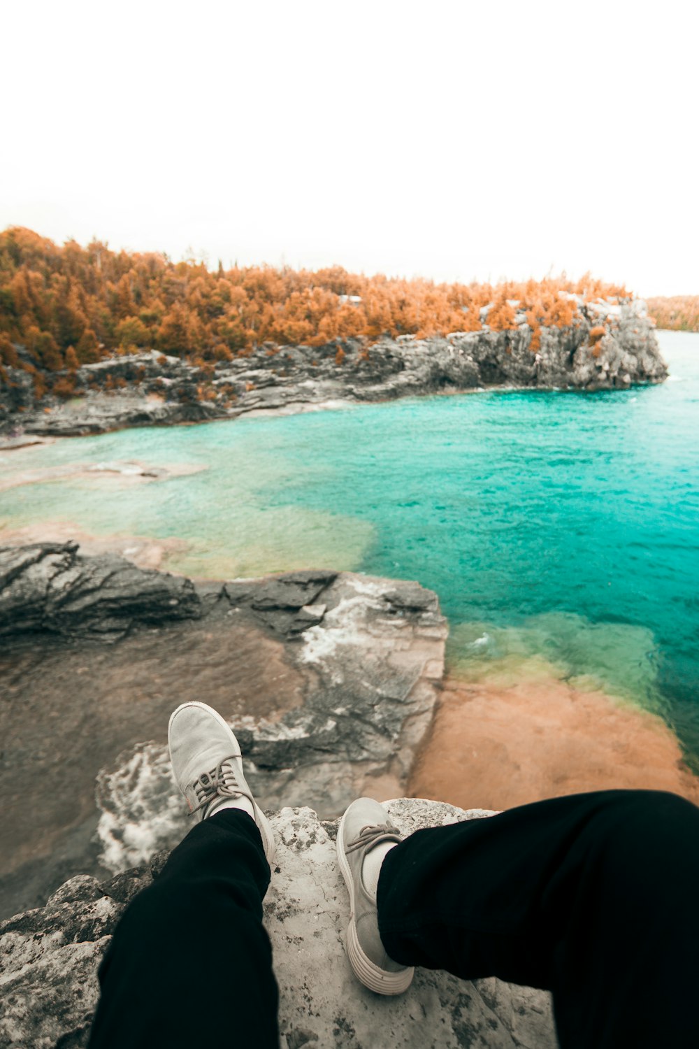 person sitting on cliff viewing body of water during daytime