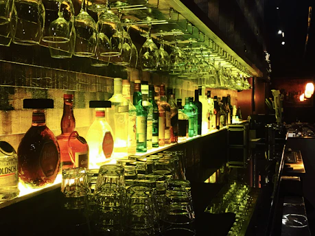 A cozy bar shelf lined with various bottles of red wine glowing softly under warm lighting.
