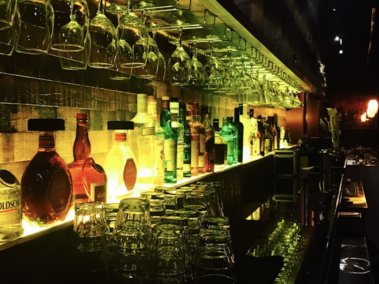 A cozy, warmly lit bar scene featuring a wooden door painted red, with shelves of elegant wine bottles glowing softly in the background.