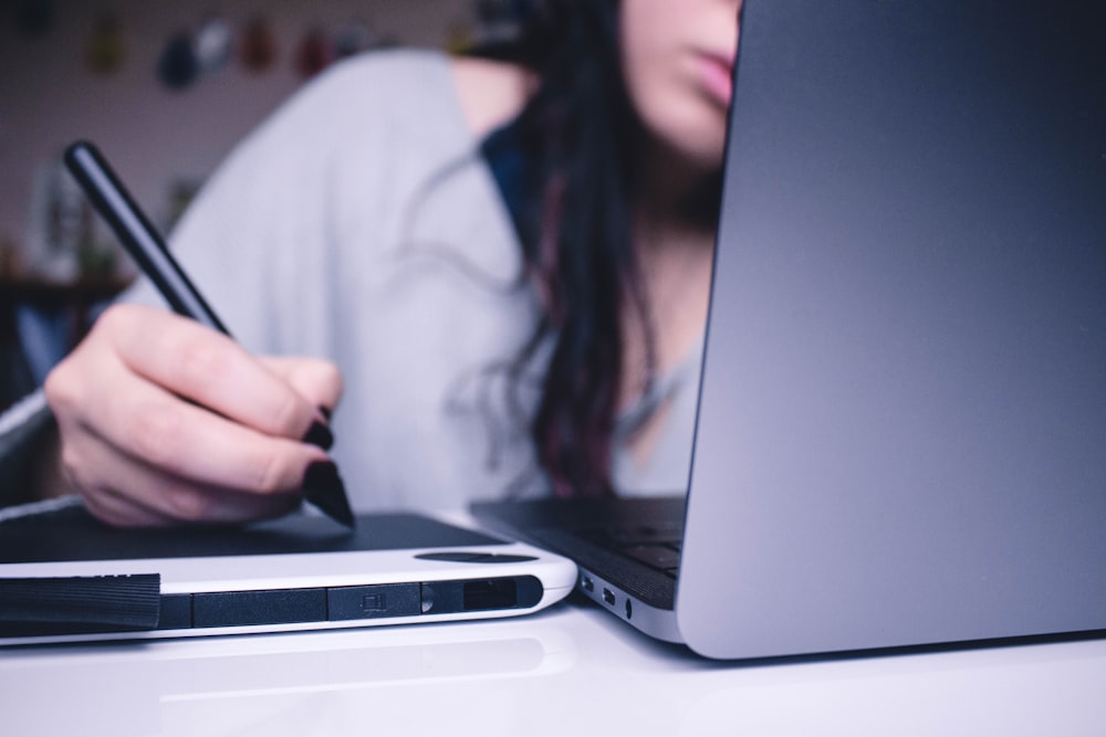 Frau benutzt Zeichenblock, während sie vor dem Laptop sitzt