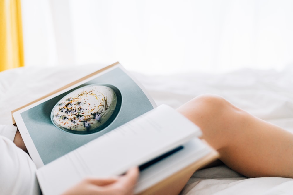 person holding open magazine while laying on bed