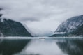 white and gray boat in the middle of calm body of water near mountain under white sky