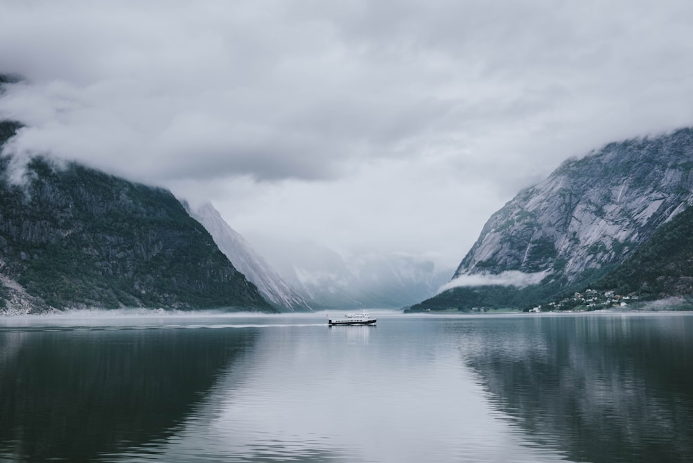 white and gray boat in the middle of calm body of water near mountain under white sky