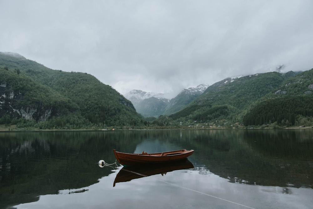 barca marrone sullo specchio d'acqua vicino alle montagne verdi sotto il cielo bianco durante il giorno