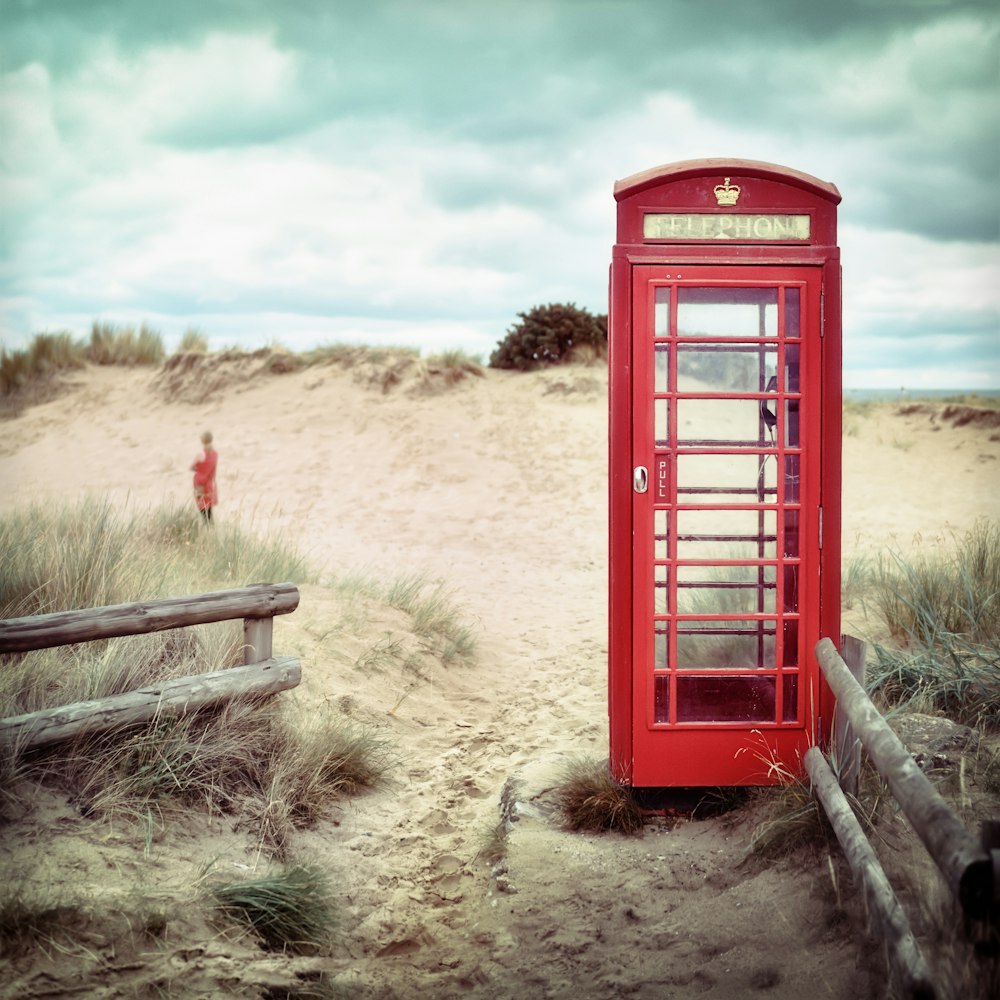 A red telephone booth sitting on a beach.