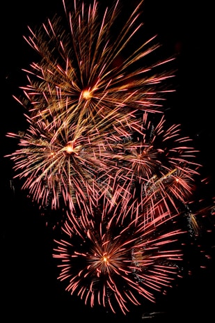 A vibrant burst of red and gold fireworks lighting up a dark night sky above a festive crowd.