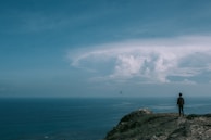 A traveler standing on a cliff overlooking a vast ocean.