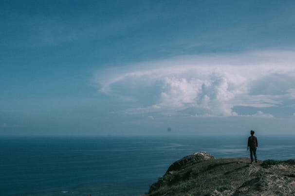 A person standing on a cliff, looking out over a vast ocean.