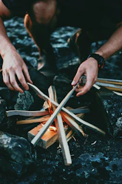 Close-up of hands crafting a fire using traditional flint and steel in a woodland setting.