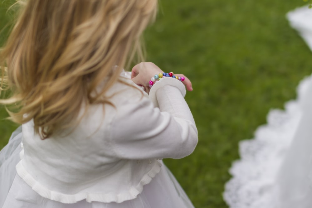 girl wearing white dress holding her bracelet