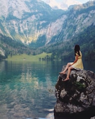 woman sitting on rock near lake