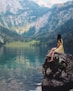 woman sitting on rock near lake