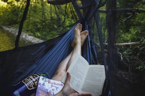 A colorful hammock tied between two trees with a book and a cold drink resting on it