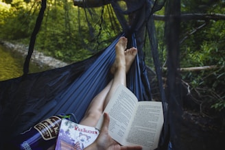 A colorful hammock tied between two trees with a book and a cold drink resting on it