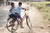two boy riding on red step-through bicycle during daytime