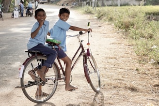 two boy on a bicycle stopping and smiling during daytime