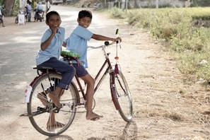 two boy riding on red step-through bicycle during daytime