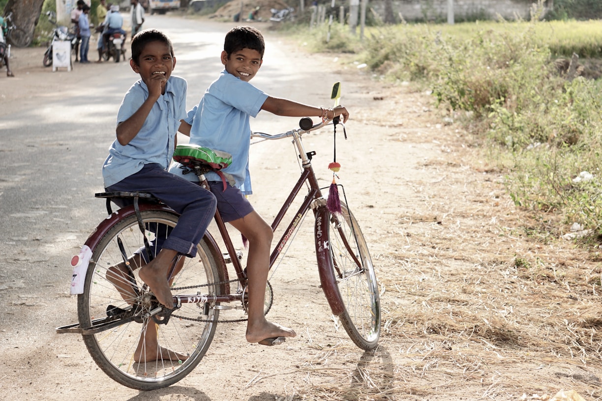 two boy on a bicycle stopping and smiling during daytime