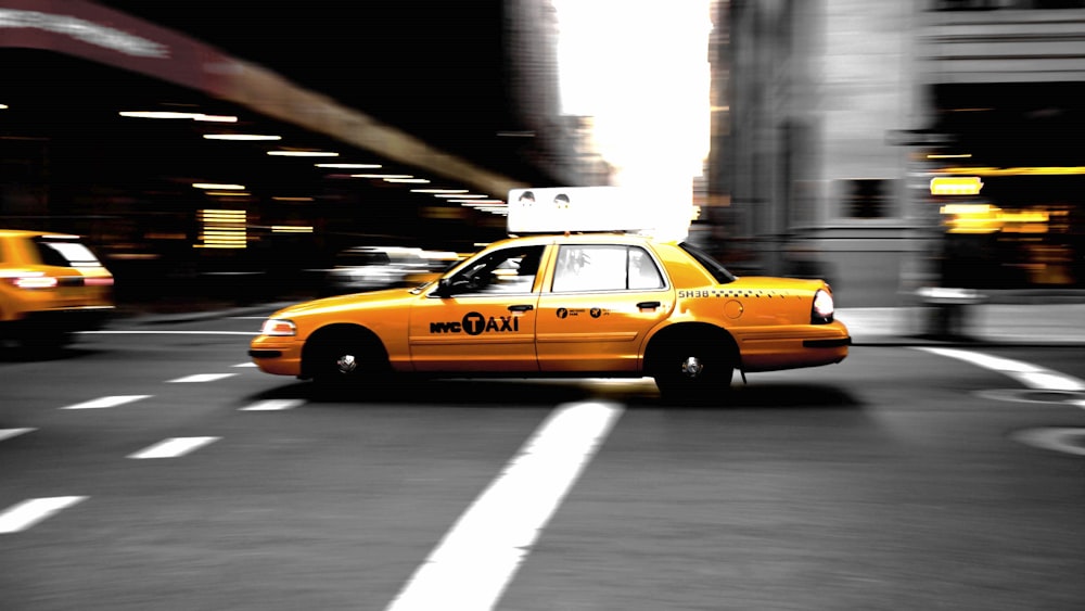 panning photography of yellow taxi on road