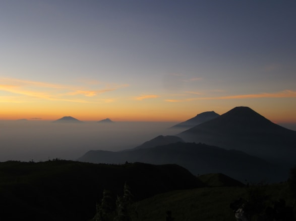 A serene mountain landscape at dawn with soft light filtering through mist.