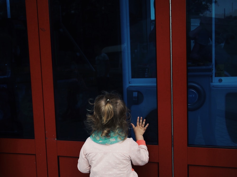 back of toddler girl looking through closed black glass wall