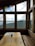 A wooden table with a map, a cup, and some papers is placed in front of large windows that offer a scenic view of mountainous terrain and partially cloudy skies. Colorful flags hang across the top of the window.