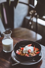 bowl of cereal with strawberries beside glass of milk on table