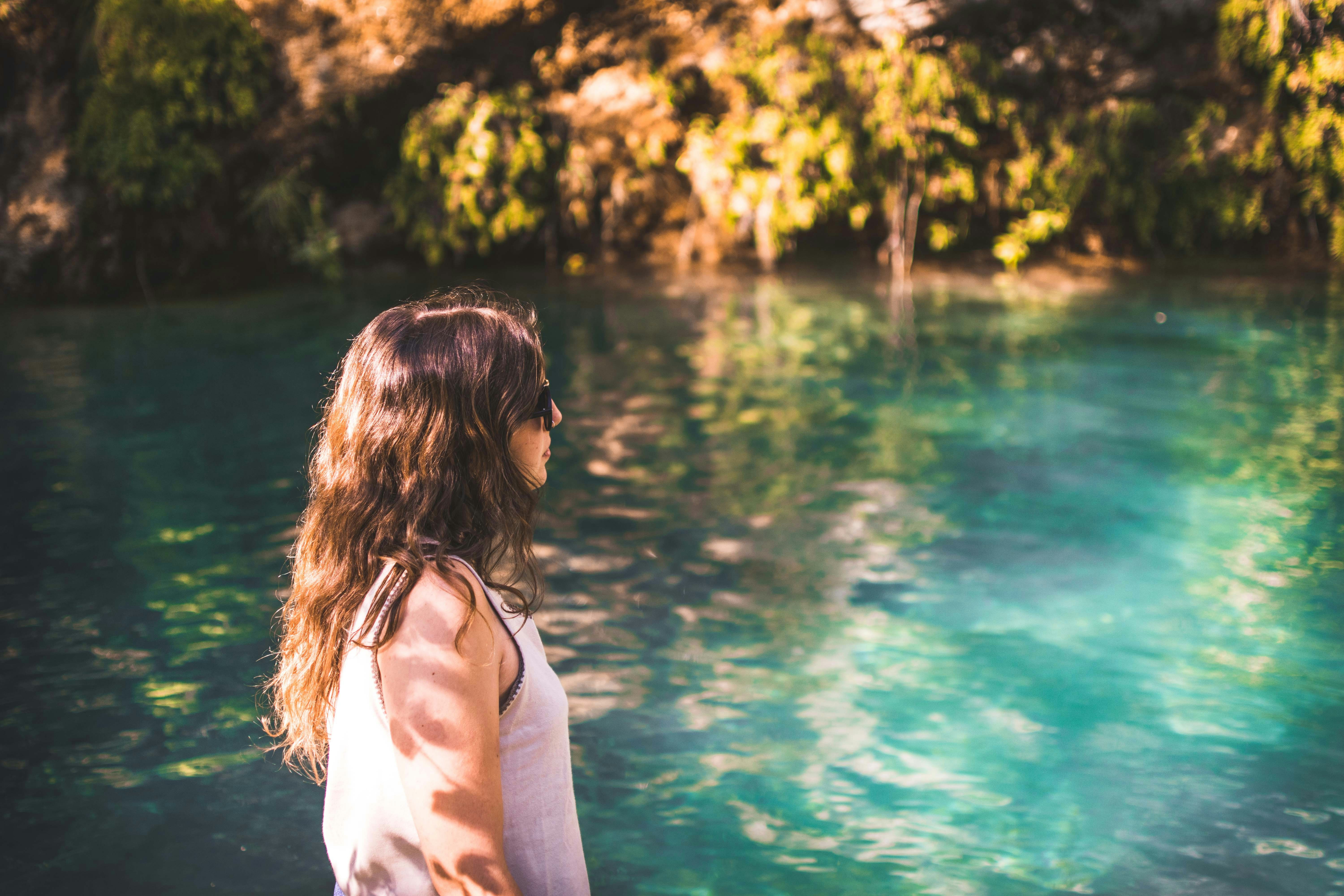 woman wearing white tank top walking beside body of water during daytime