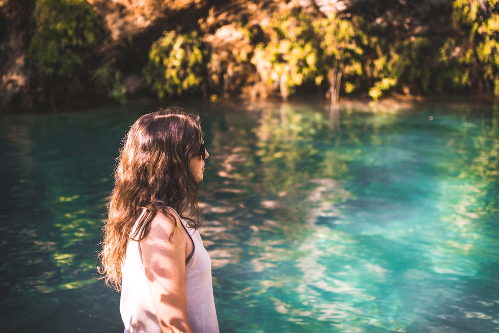 woman wearing white tank top walking beside body of water during daytime