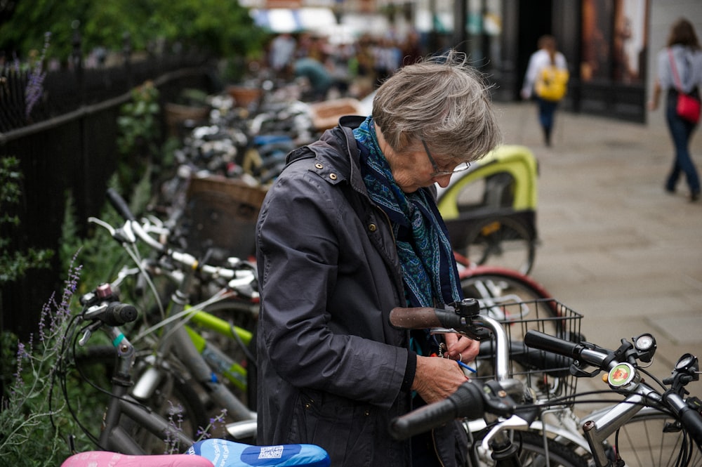 昼間、商業ビルの近くで灰色の自転車の横で黒いジップアップジャケットを着た浅い焦点の写真撮影女性