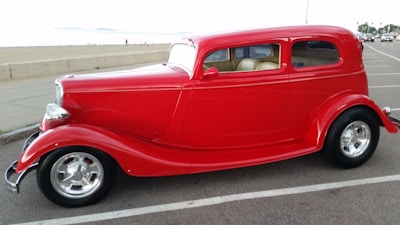 A vibrant red compact car with shiny chrome details on a coastal road.