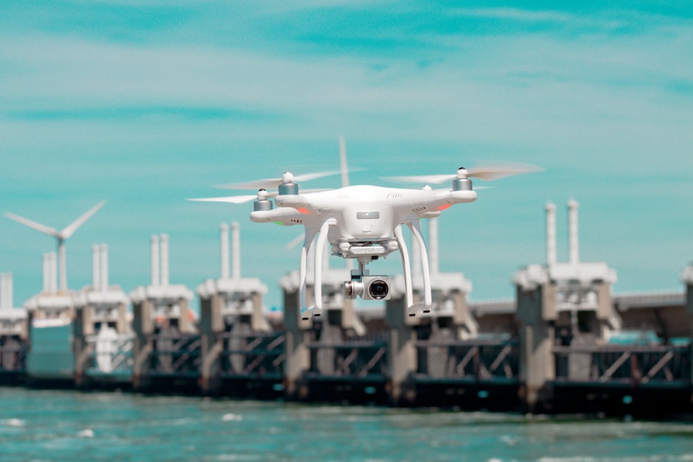 Fotografia a fuoco selettiva del drone bianco che si libra sopra lo specchio d'acqua