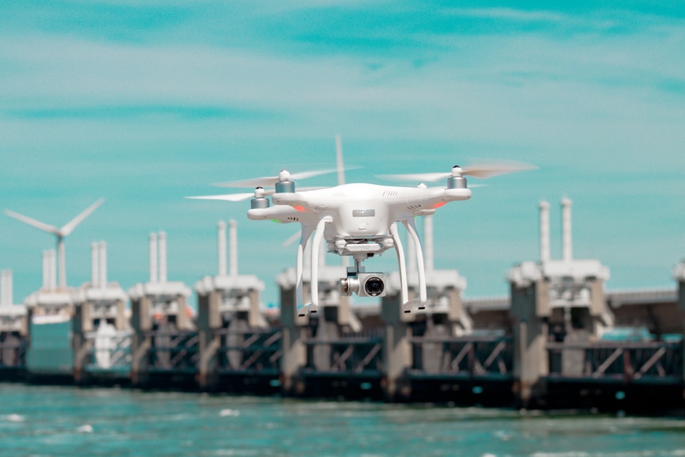 selective focus photography of white drone hovering above body of water