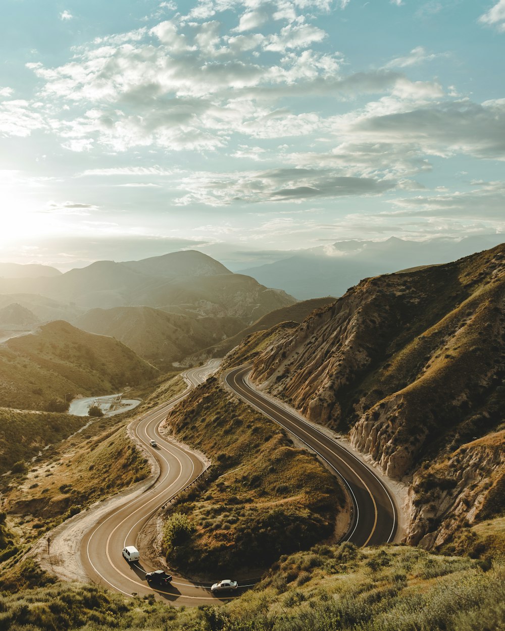 road in between hill under white clouds and blue sky