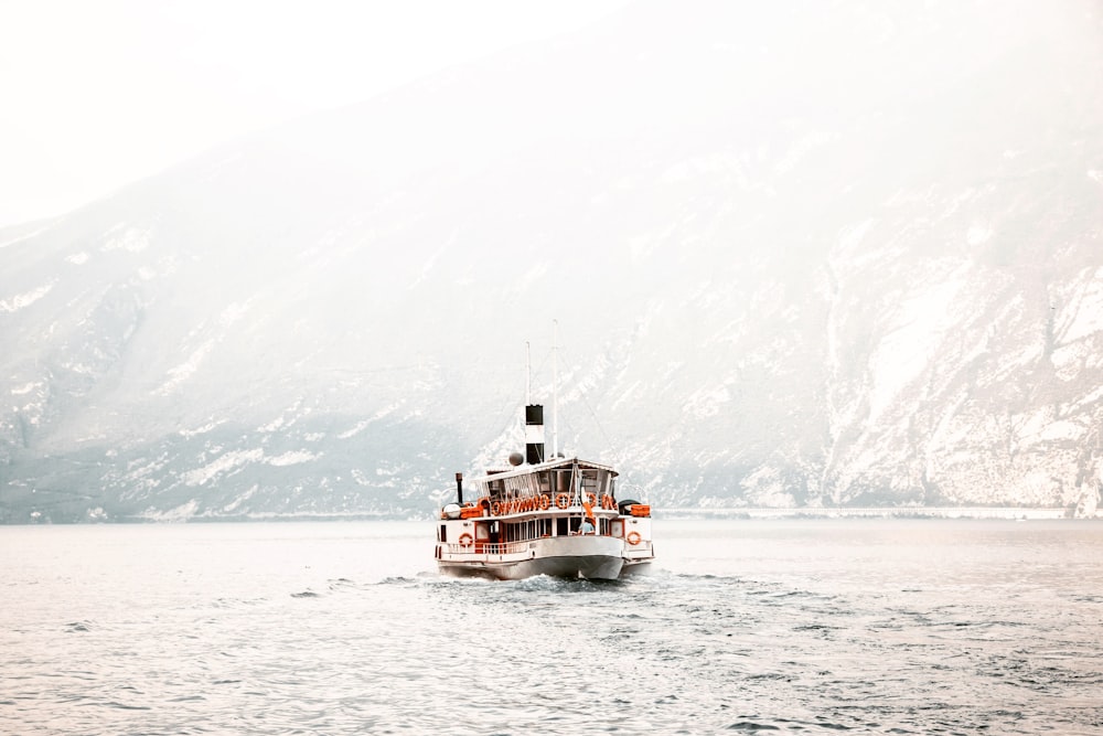 white and black ship on calm body of water near mountain