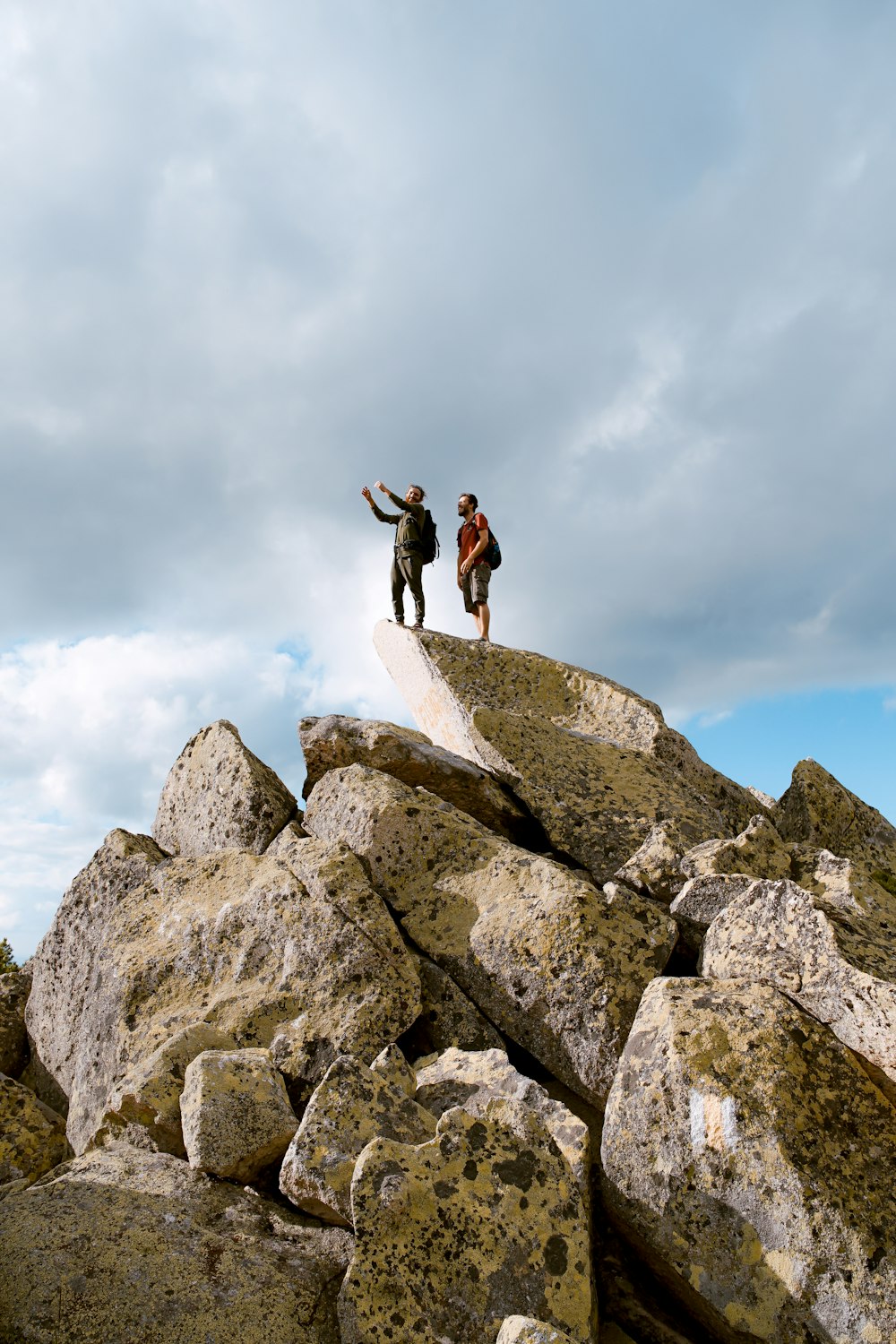 Due persone in piedi sulla roccia grigia sotto le nuvole bianche