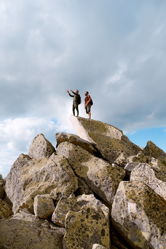 two people standing on grey rock under white clouds in Retezat National Park Romania