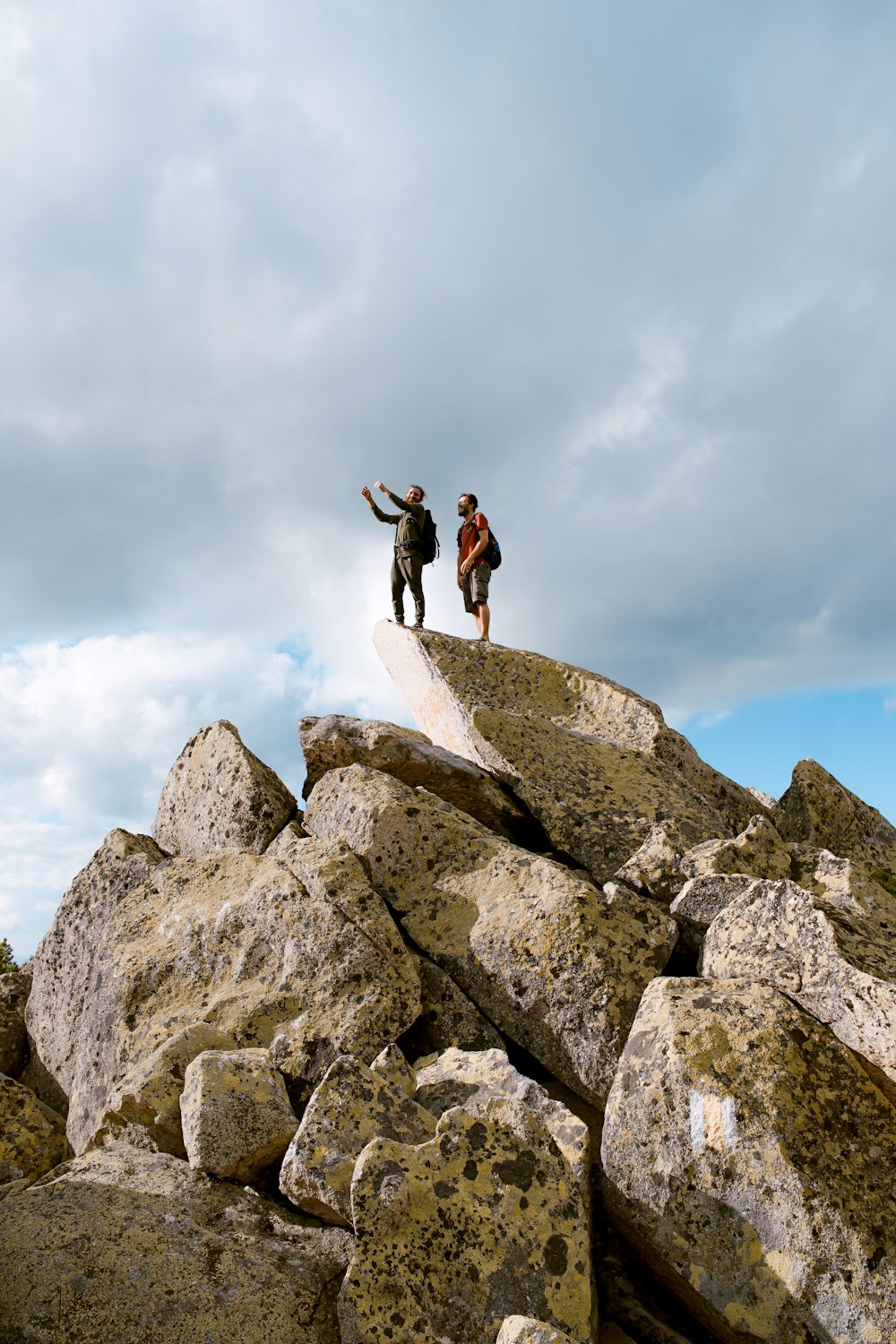 흰 구름 아래 회색 바위 위에 서 있는 두 사람