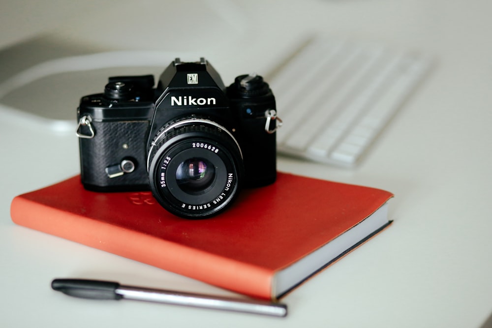 cámara Nikon MILC negra en libro y bolígrafo rojos