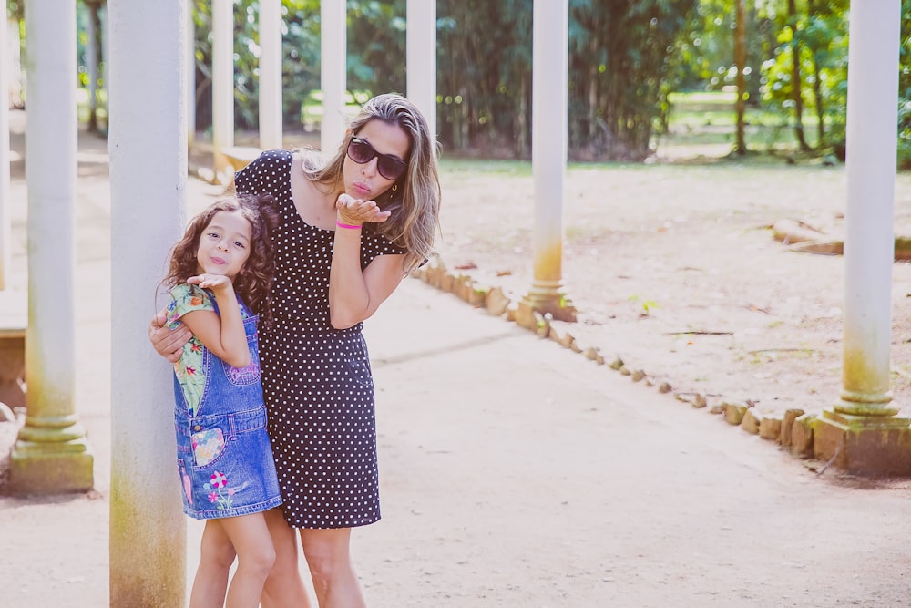 A woman puts her arm around a young girl, and both blow kisses